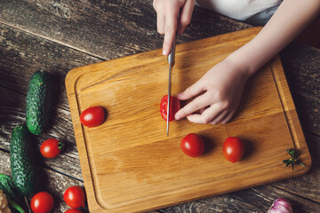 Chef is cutting vegetables for salad on a chopping board, top view. Son preparing healthy food for family dinner