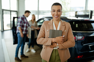 Wall Mural - Smiling saleswoman holding tablet while looking at camera at car showroom.