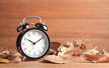 black alarm clock and dry leaf on wood background with copy space , time and wilted concept