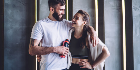 Cheerful young couple in love training together in gym enjoying healthy lifestyle and losing weight, smiling caucasian female hugging satisfied with workout results smiling and training muscles