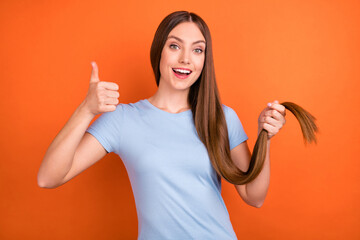 Wall Mural - Photo of optimistic brown hairdo millennial lady show thumb up wear blue t-shirt isolated on vivid orange color background