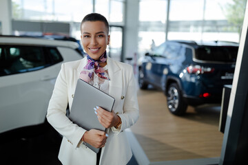 Wall Mural - Saleswoman in car showroom holding a laptop computer and selling cars.