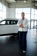 Wall Mural - Full length photo of smiling saleswoman in car showroom holding a laptop computer and selling cars.