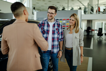 Wall Mural - Saleswoman and customer shaking hands congratulating each other at the dealership showroom.