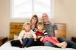 © Jennifer Bogle/Stocksy - Family poses on a bed smiling at the camera