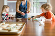 © Jennifer Bogle/Stocksy - Children decorate sugar cookies at kitchen table with mom