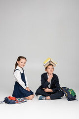 Wall Mural - pensive schoolboy with books on head sitting near cheerful girl on grey.