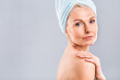 © denis_vermenko - Portrait of smiling senior woman feeling soft skin with hand after spa bath. Mature woman draped in towel looking at camera. Lady in bathrobe after shower isolated over white background.