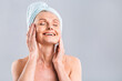 © denis_vermenko - Portrait of smiling senior woman feeling soft skin with hand after spa bath. Mature woman draped in towel looking at camera. Lady in bathrobe after shower isolated over white background.