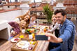 © VICTOR TORRES/Stocksy - Cheerful family taking selfie during breakfast on terrace