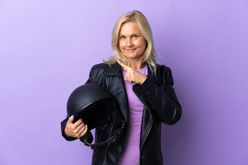 Wall Mural - Middle age woman holding a motorcycle helmet isolated on purple background pointing to the side to present a product