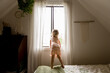 © Jennifer Bogle/Stocksy - Girl stands on bed peering out window