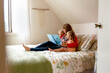 © Jennifer Bogle/Stocksy - Mother sits on bed reading to daughters