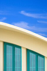 Wall Mural - Green glass attic windows on curved roof of modern yellow building against white cloud and blue sky background in vertical frame