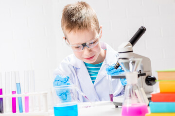 Wall Mural - a schoolboy with a microscope examines chemicals in test tubes, conducts experiments - a portrait on