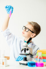 Wall Mural - a schoolboy with a microscope examines chemicals in test tubes, conducts experiments - a portrait on
