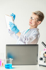 Wall Mural - schoolboy with a laptop in the laboratory conducts chemical experiments with substances in test tube