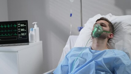 the man lies on the bed in the hospital in oxygen masks and regains consciousness. connected to the 