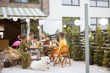 A group of young friends and dog have delicious dinner, having great summertime together at the backyard of the country house