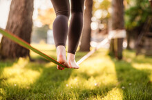 Slacklining Is A Practice In Balance That Typically Uses Nylon Or Polyester Webbing. Girl Walking On A Slackline In A Park During A Sunset. Slack Line