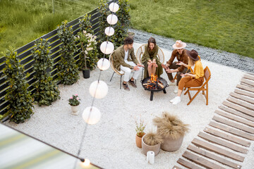 A group of young friends having great summertime, sitting by a fireplace at the backyard of the country house in nature. Top view