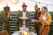Young adult friends celebrating birthday, having fun blowing candles on a cake at backyard of a country house outdoors