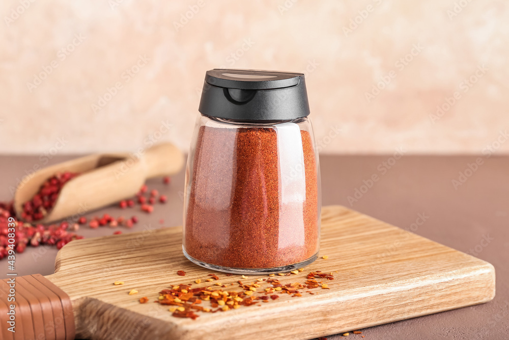 Jar with red pepper powder and peppercorns on color background