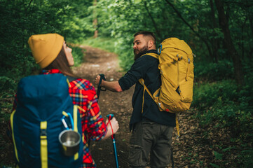 Couple of hikers walking in the nature with trekking poles and wearing backpacks