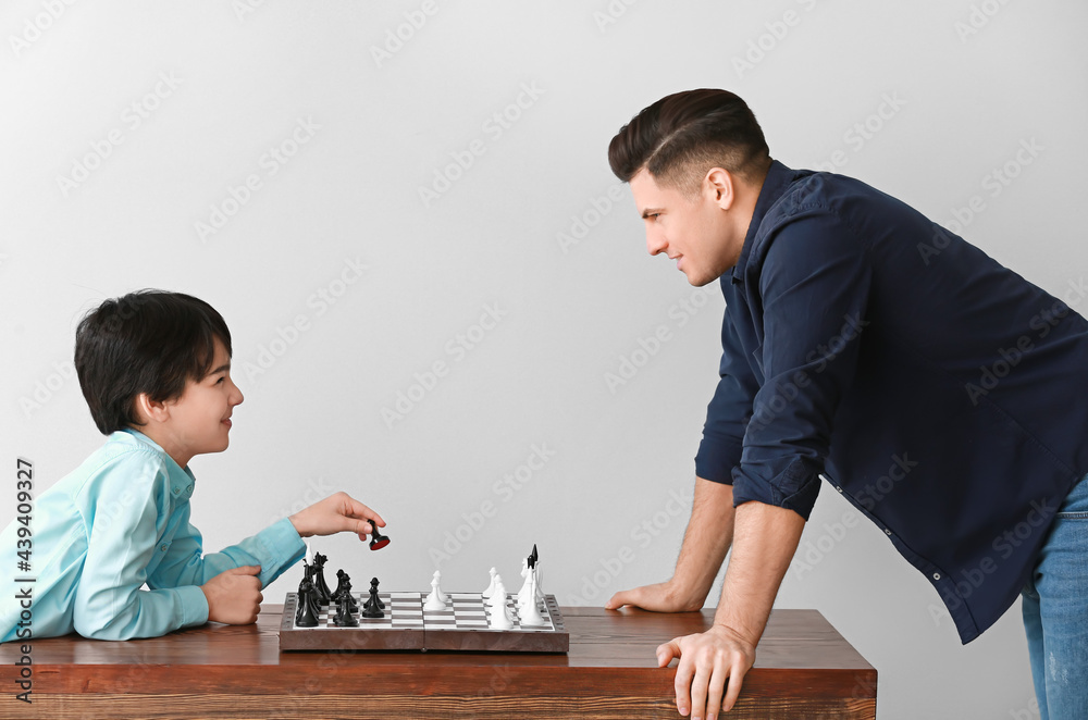 Father and son playing chess on light background