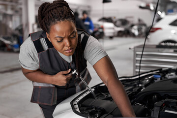 Wall Mural - African Female Checks an Engine Breakdown. Car Service Employee Woman Fix the Engine Component. Modern Clean Workshop. Black Woman In Overalls Looks Concentrated