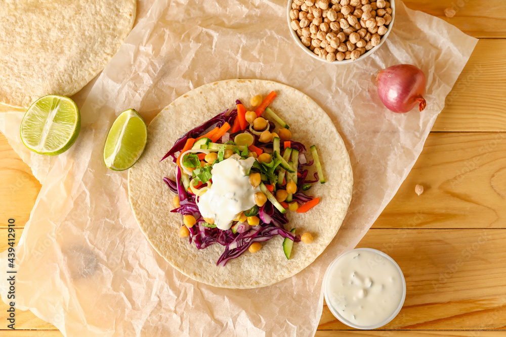 Parchment with tasty vegetarian taco on wooden background