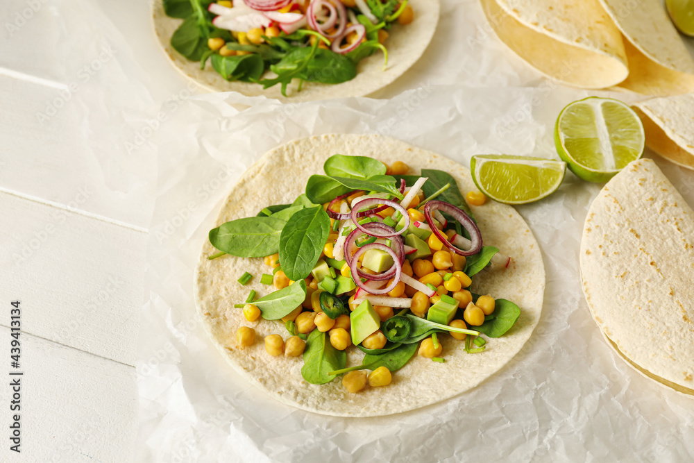 Parchment with tasty vegetarian tacos on light wooden background