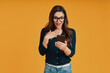 © gstockstudio - Shocked young woman in casual clothing using smart phone while standing against yellow background