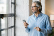 © Mihajlo Ckovric/Stocksy - Portrait of a confident senior businessman using his cell phone in the office