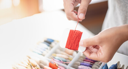 Wall Mural - Close up hands of tailor woman holding orange threads and different colors in the box put on table and prepare to use with white cotton and frame wood.