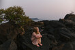 © Amanda Voelker/Stocksy - A young girl on rock in the ocean at sunset