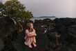 © Amanda Voelker/Stocksy - A young girl on rock in the ocean at sunset