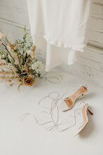 Wedding Dress, Flower Arrangement And High Heel Open Toe Shoes On White Floor