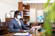 © JackF - African american businessman wearing protective face mask focused on working with laptop in modern office. Necessary precautions during coronavirus pandemic