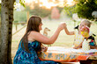 © Jennifer Bogle/Stocksy - Mother and daughter clink cups at picnic table