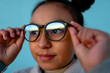 © Jimena Roquero/Stocksy - Pre-teen putting on glasses over blue background