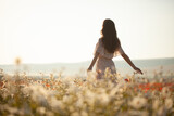 Fototapeta Dmuchawce - Beautiful girl in summer dress walks in a flower field