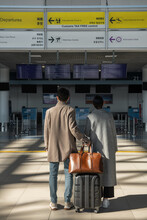 Anonymous Couple With Luggage Reading Signs In Airport