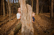 © Jakob Lagerstedt/Stocksy - Brother and sister peeking out from behind a tree trunk