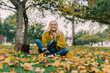 © Eloisa Ramos/Stocksy - Senior woman sitting on the park floor holding dry leaves and looking at camera