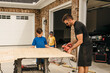 © Jessica Klaus/Stocksy - Dad working on a woodworking project with the help of his kids.
