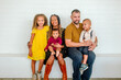 © Erin Brant/Stocksy - Happy biracial family seated on ledge in front of white wall
