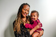 © Erin Brant/Stocksy - Laughing african-american mom with long  braids holding smiling biracial daughter