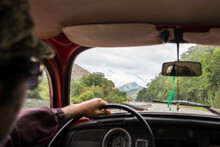 Point Of View Of A Man Wearing A Hat And Sunglasses Driving A Red Vintage Car In The Mountains