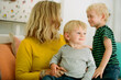 © Erin Brant/Stocksy - Cute young blond-haired boy on mother's lap indoors with old brother nearby